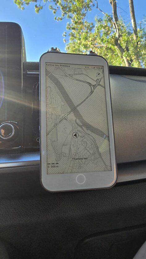 The LilyGo T5 E-Paper S3 Pro clipped to a car dashboard mount in direct morning sunlight, its panel showing an ExplorInk map with every line legible and no backlight
