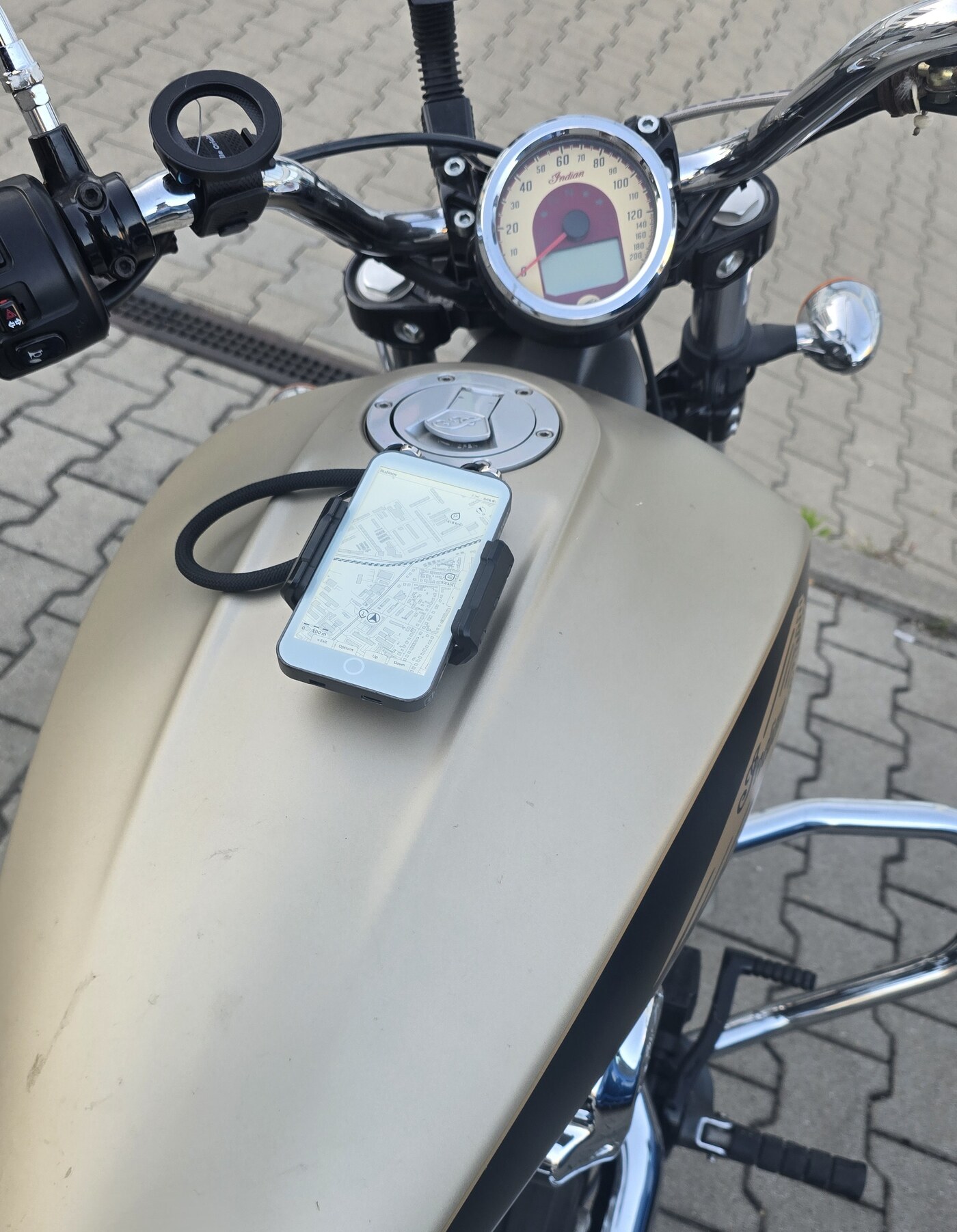 Wider view of the same parked cruiser from the rider's seat: handlebars, mirror and the bike's own analogue speedometer, with the LilyGo board flat on the fuel tank showing its map